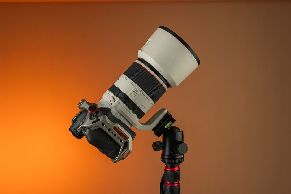 Câmera mirrorless com lente telephoto zoom branca montada em tripé contra fundo laranja
